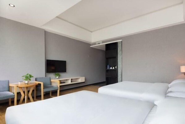 Quarto de hotel com cama, televisão, área de estar com cadeiras e mesa, e guarda-roupa.