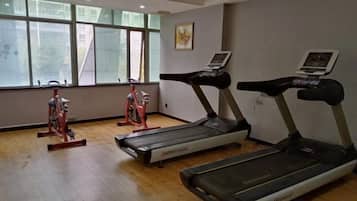 A gym with treadmills and stationary bikes, large windows, and a wooden floor.
