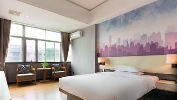 A hotel room with a large bed, a cityscape mural, a seating area with chairs and a table, and large windows.
