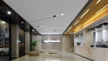 A modern hotel lobby with a reception desk, seating area, and a large window overlooking the street.
