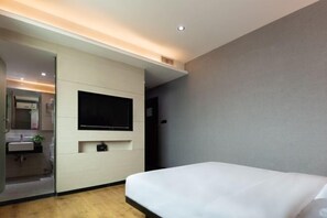 A modern hotel room with a bed, a mounted TV, a small bedside table, and a bathroom visible through a glass partition. - Caiyang Hotel (Haifeng)