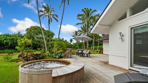 Une terrasse en bois dotée d’un jacuzzi, de mobilier d’extérieur et offrant une vue sur un jardin luxuriant agrémenté de palmiers.