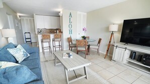 Een woonkamer met een bank, een salontafel, een televisie en een eethoek met stoelen en een tafel.
