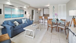 Een moderne woonkamer met een blauwe bank, een salontafel, en een eethoek met rieten stoelen en een ronde tafel.