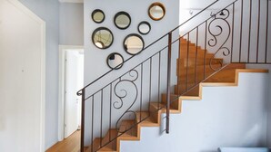A staircase with wooden steps and a metal railing, leading to a room with a light blue wall and several round mirrors on the wall. - Sky 2BR Penthouse by HolyGuest (Tel Aviv)