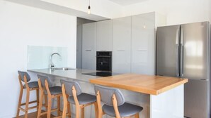 A modern kitchen with a central island, bar stools, a stainless steel refrigerator, and a built-in oven. - Sky 2BR Penthouse by HolyGuest (Tel Aviv)