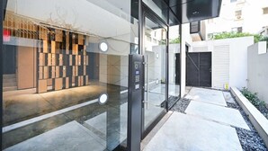 Une entrée moderne avec une porte en verre, un système d’accès par clavier et un chemin menant à une zone protégée par une grille.