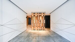 Un couloir moderne avec un motif géométrique au sol, une cloison centrale en bois et un escalier en arrière-plan.