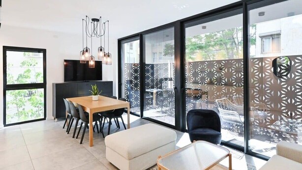Un salon moderne avec une table à manger en bois, des chaises noires, un canapé blanc et une table basse en verre.