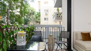 Een balkon met een glazen tafel, twee stoelen, een witte lantaarn en een bank.