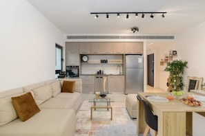 A modern kitchen with stainless steel appliances, a dining area with a wooden table and chairs, and a living area with a sofa and coffee table.