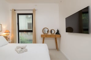 Une chambre d’hôtel comprenant un lit, une table de chevet agrémentée de petits miroirs décoratifs, un téléviseur fixé au mur et une fenêtre avec des rideaux.