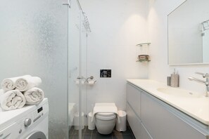A modern bathroom with a glass shower enclosure, a washing machine, a toilet, and a sink with a mirror.