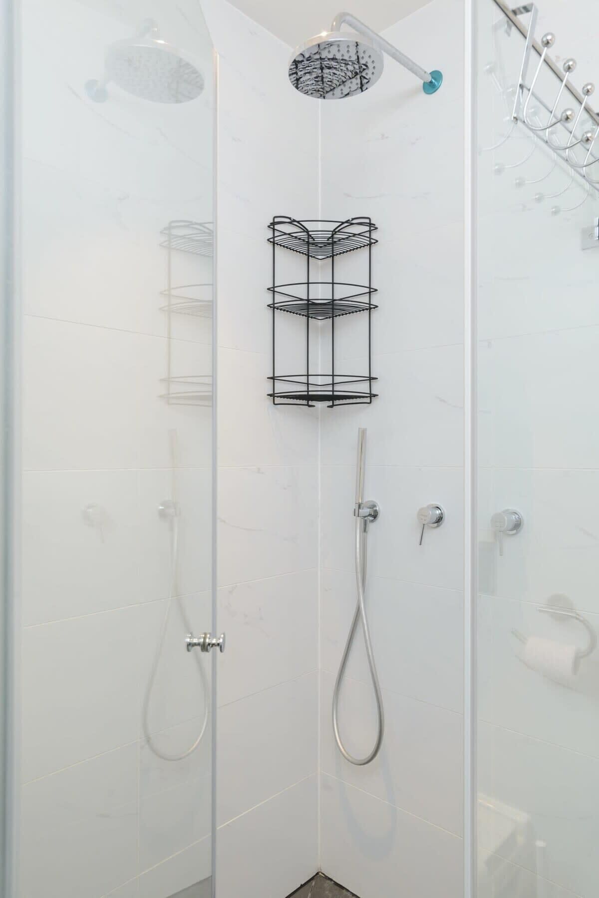 Cabina de ducha con paredes de vidrio, ducha de mano, toallero adherido a la pared y organizador para artículos de baño.