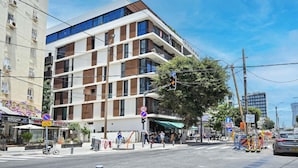 Een meerhoog gebouw met een modern ontwerp, met een combinatie van glazen en houten geveldelen, gelegen op een hoek van een straat met zichtbare bewegwijzering en een heldere lucht.