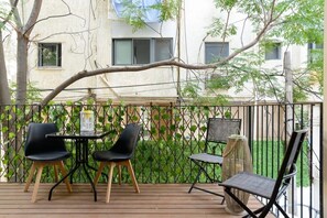 A balcony with a table and chairs, surrounded by a metal fence and greenery.