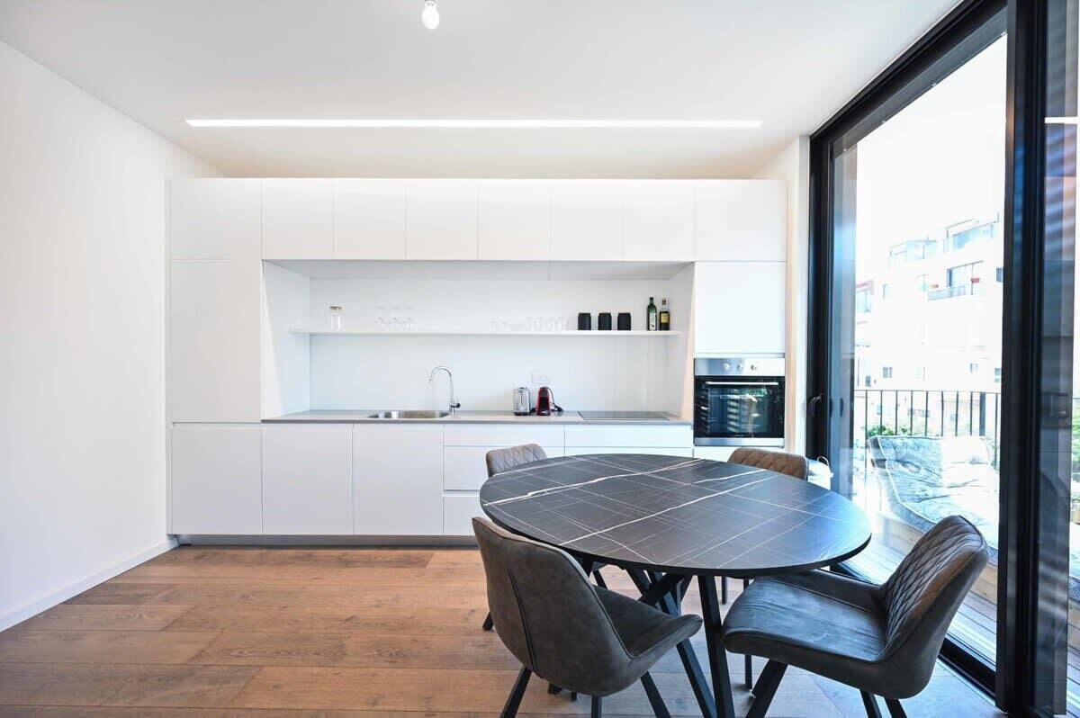 A modern kitchen with white cabinets, a black dining table, and a large window offering a view of the outside.