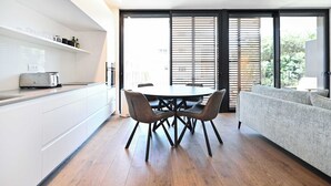 A modern kitchen with white cabinetry, a dining table with four chairs, and a grey sofa.