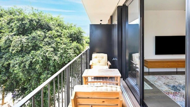 A balcony with a wooden table and chairs, a flat-screen TV, and a view of lush greenery.