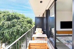A balcony with a wooden table and chairs, a flat-screen TV, and a view of lush greenery. - Charming 2BR with Balcony in Ben Yehuda st By HolyGuest (Tel Aviv)