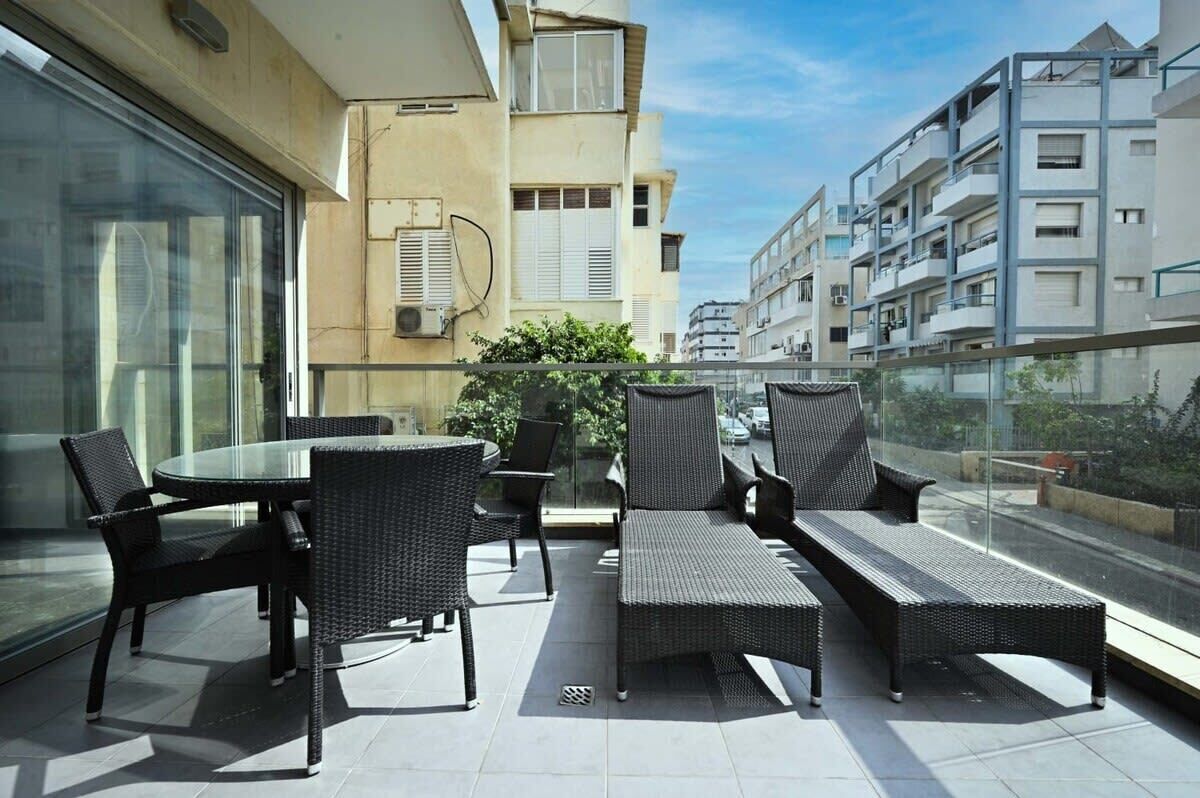 A balcony with wicker furniture, a glass table, and a view of adjacent buildings.