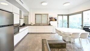 A modern kitchen with white cabinetry, a built-in oven, and a large island with a sink. - Mamma Mia 3BR in Frishman beach by HolyGuest (Tel Aviv-Yafo)