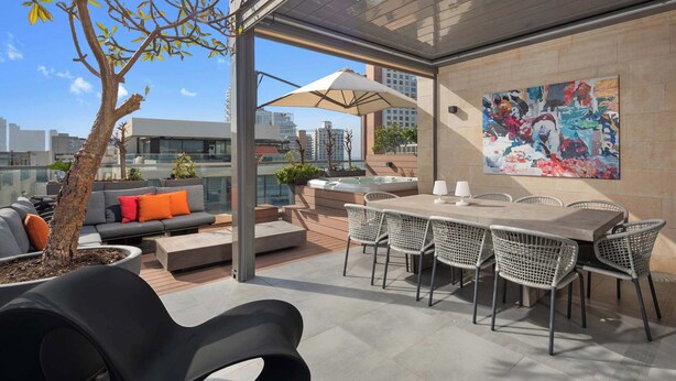 Une terrasse sur le toit comprenant un espace repas, des sièges d’extérieur, un jacuzzi et une grande peinture abstraite sur le mur.
