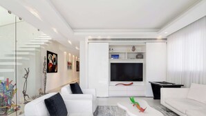 Un salon moderne avec des meubles blancs, un téléviseur à écran plat et des œuvres d’art abstraites accrochées aux murs.