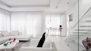 Un salon moderne avec un canapé blanc, un escalier en verre et un coin repas doté d’une table en verre.