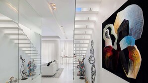 Un intérieur moderne avec un escalier, des meubles blancs et des œuvres d’art abstraites.