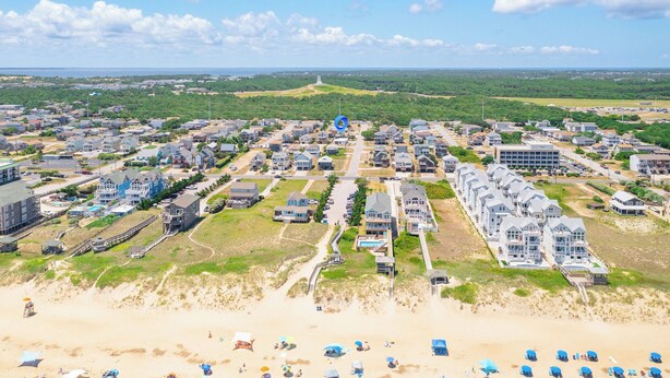 Vista aérea de una zona residencial costera con casas, una playa y un faro a lo lejos.