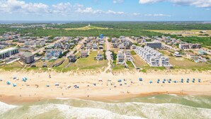 Zona residencial costera con propiedades frente al mar, un faro a lo lejos y una playa con sombrillas.