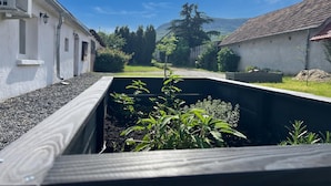 A garden bed with plants, a white building with a window, and a red-tiled roof.