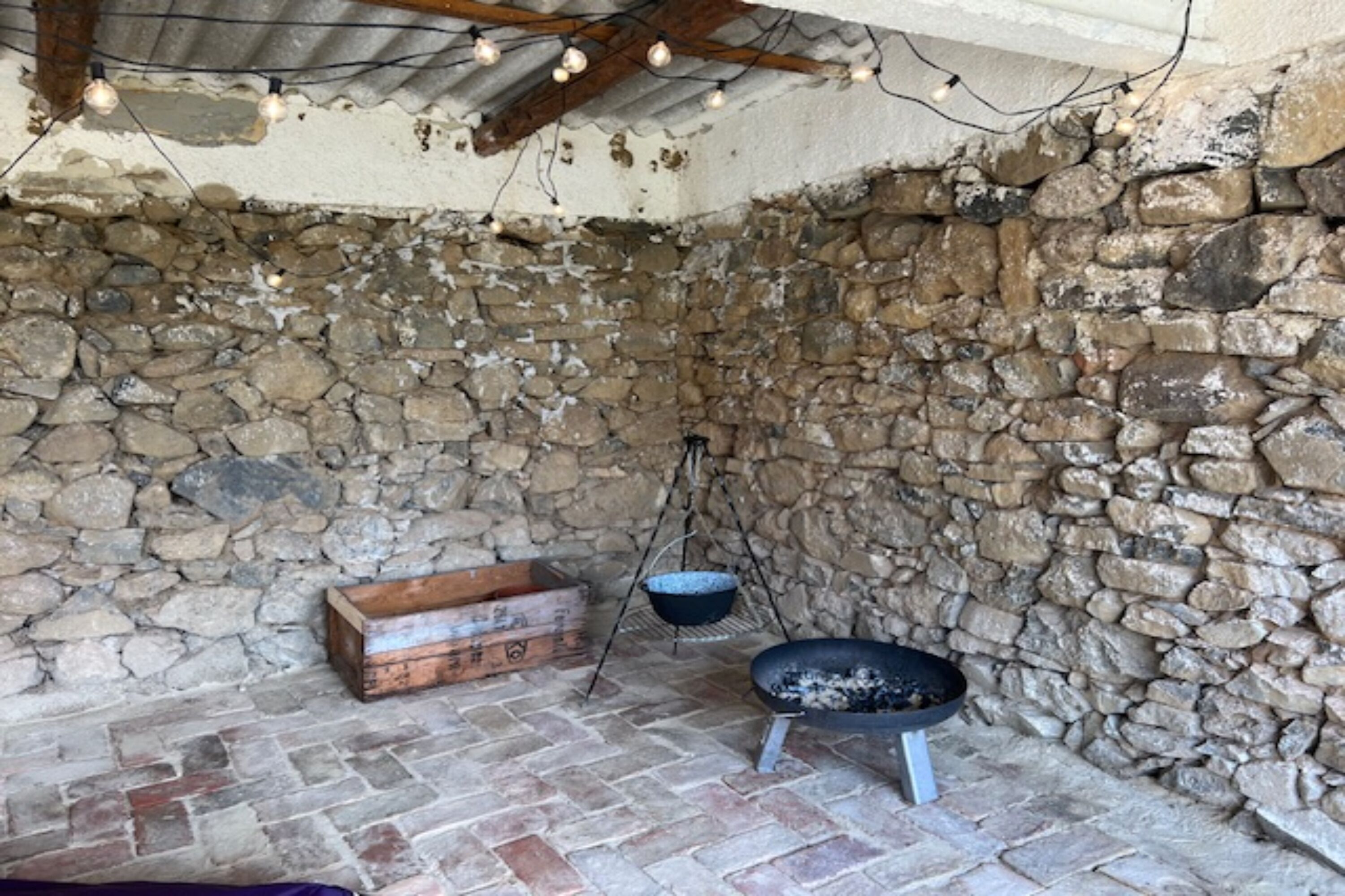 A rustic stone-walled room with a brick floor, a wooden chest, a hanging pot, and a black pan.