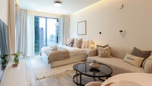 A modern hotel room with a large bed, a sofa, a glass coffee table, and a view of the city. - HiGuests - Ahad Residences (Madinat Zayed)
