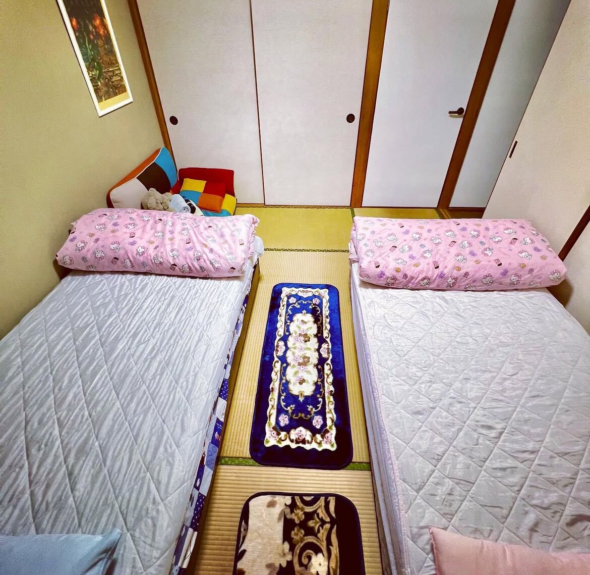 Una habitación con dos camas, cada una con un cojín rosa y una colcha acolchada. Un tapete decorativo azul se encuentra entre las camas.