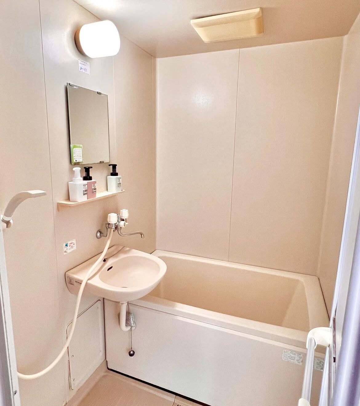 A bathroom with a bathtub, a sink, and a mirror. There are toiletries on a shelf above the sink.