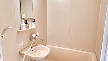 A bathroom with a bathtub, a sink, and a mirror. There are toiletries on a shelf above the sink.