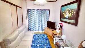 A living room with a white sofa, a blue star-patterned rug, a wooden coffee table, a television, and a Snoopy plush toy.