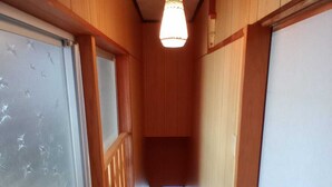 A narrow wooden hallway with a ceiling light, a door on the left, and a window at the end.