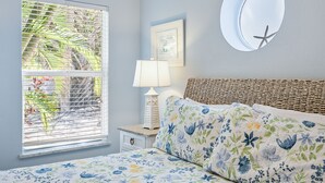 A bedroom with a bed, a nightstand, a lamp, a window with blinds, and a wall-mounted round mirror. - Beautiful villa with Private Pool, short stroll to beach w/ beach gear and grill (Holmes Beach)