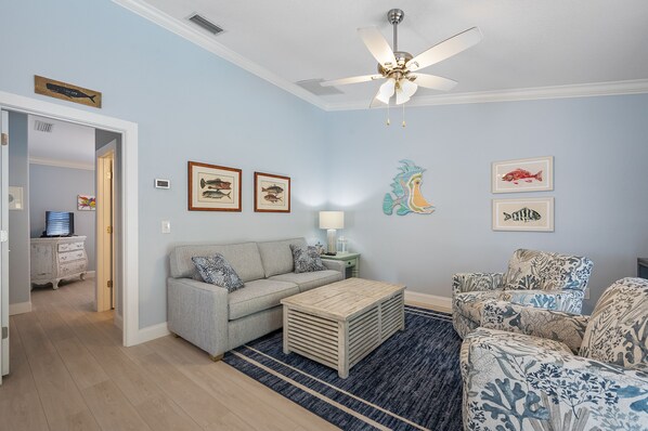A living room with a grey sofa, patterned armchairs, a coffee table, and a ceiling fan. - Beautiful villa with Private Pool, short stroll to beach w/ beach gear and grill (Holmes Beach)