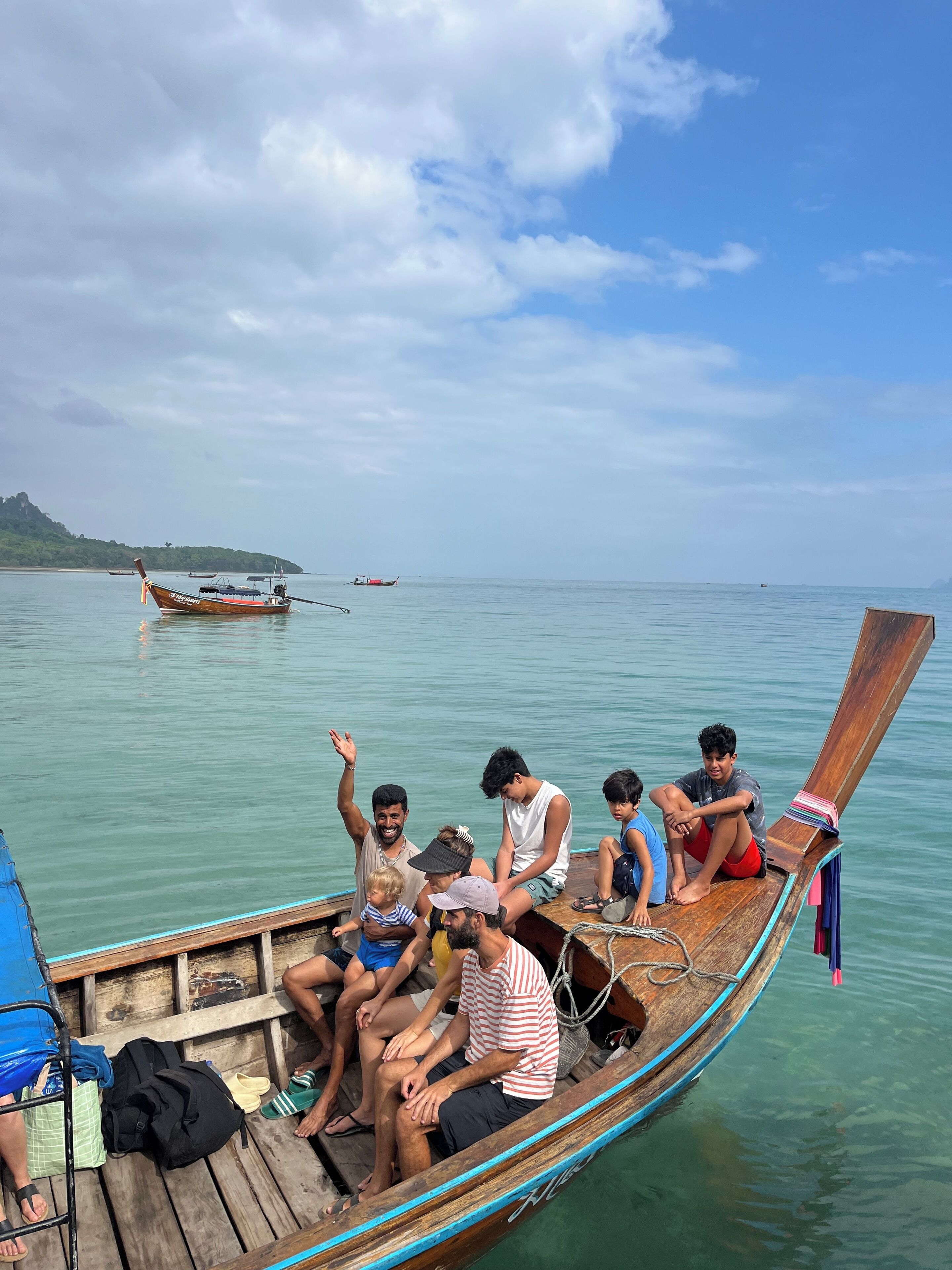 A wooden boat with people sitting on it, a calm sea, and a distant island.