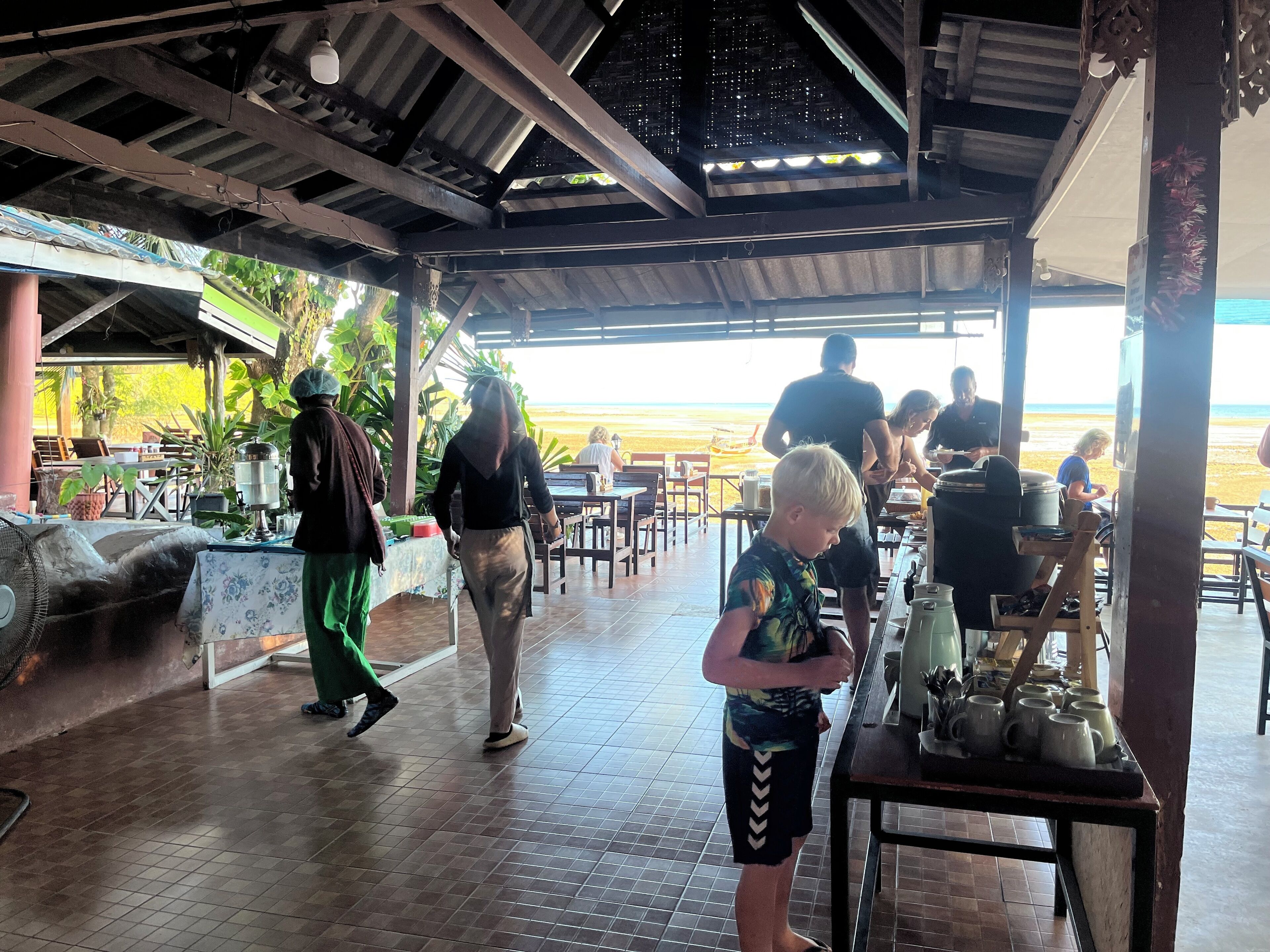 An outdoor restaurant with a view of the beach, wooden flooring, and tables with chairs.