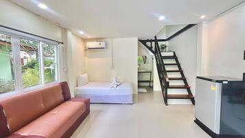 A modern living space with a sofa, a bed, a staircase, and a refrigerator.