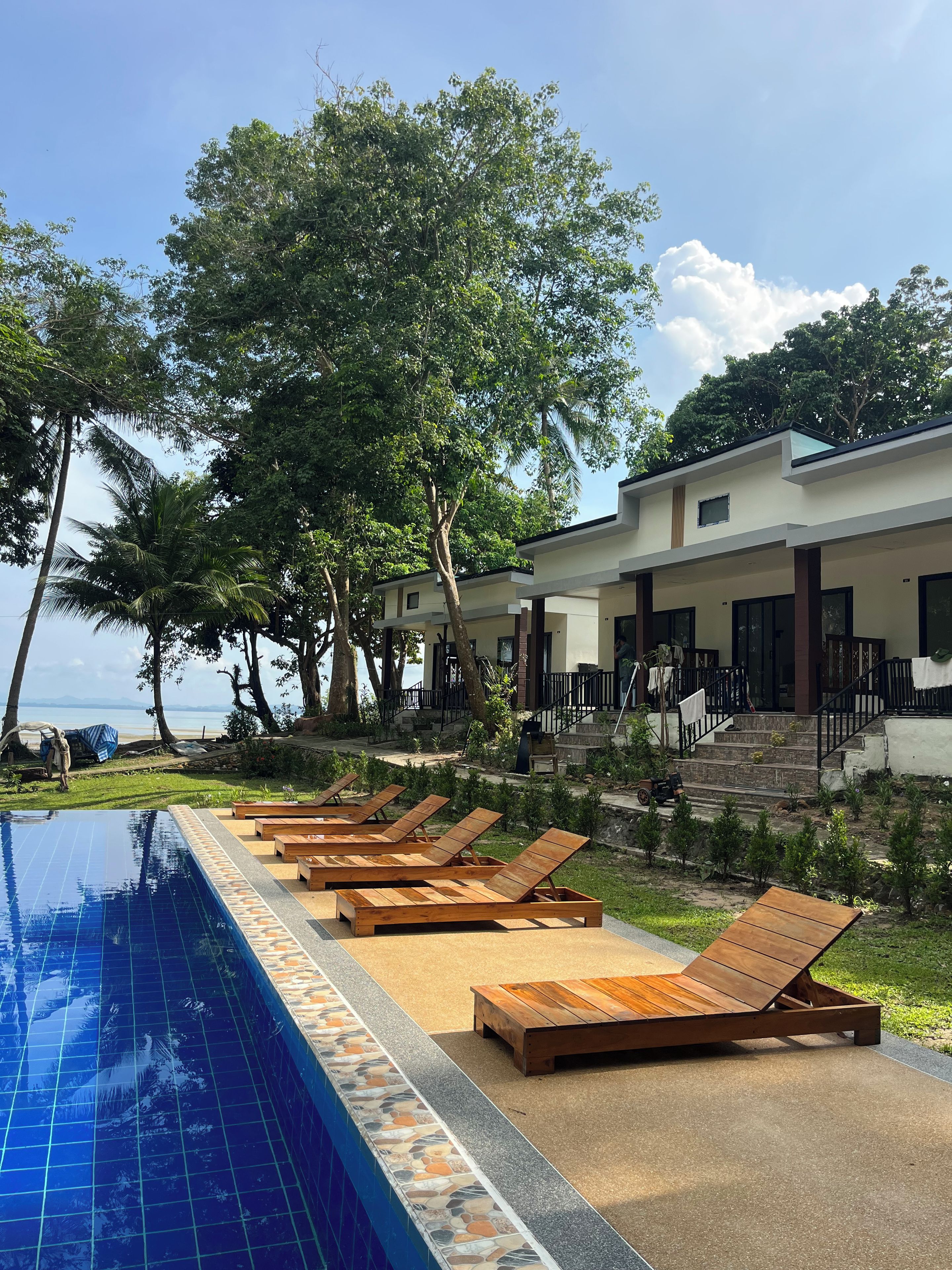A poolside area with lounge chairs, a tiled pool, and a building with a staircase.