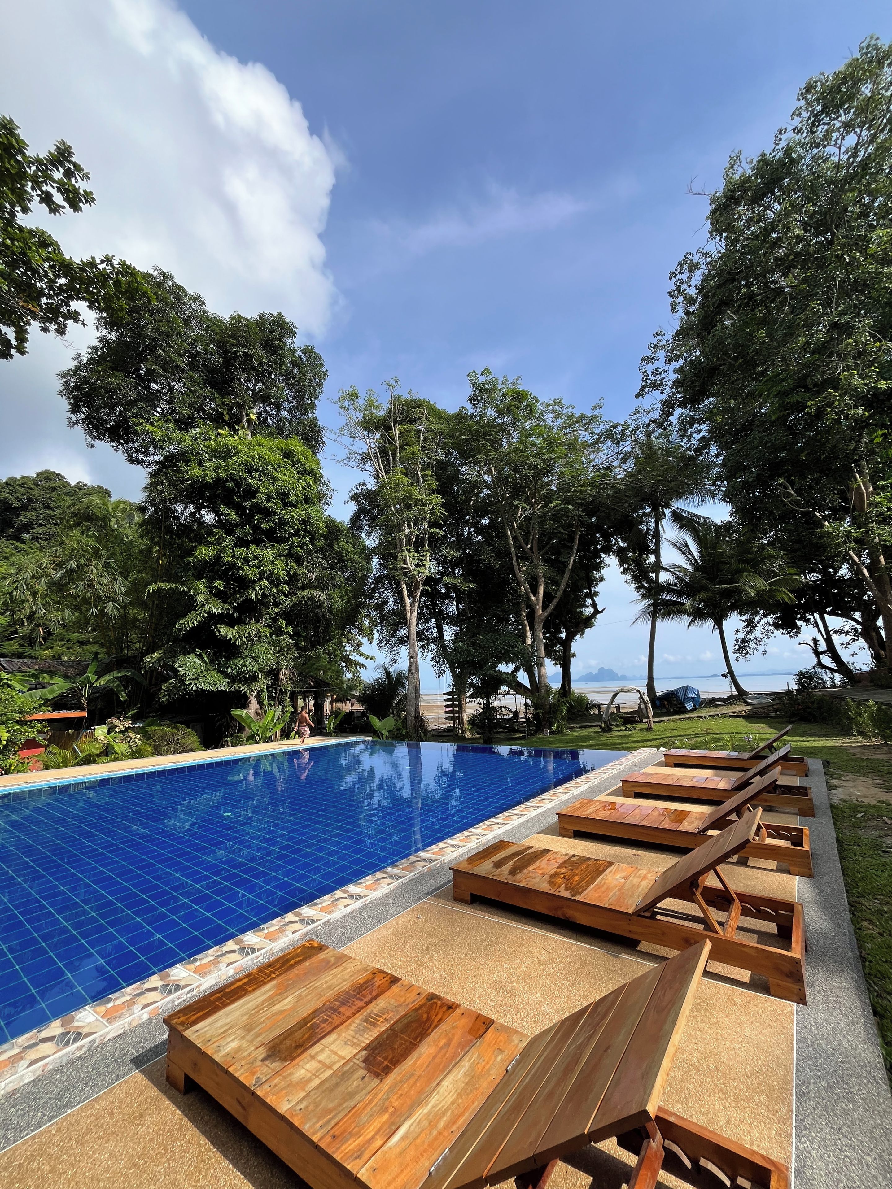 A swimming pool with wooden loungers and a view of the sea.
