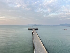 Une jetée s’avançant dans des eaux calmes, sous un ciel dégagé, avec des montagnes qui se dessinent à l’horizon.