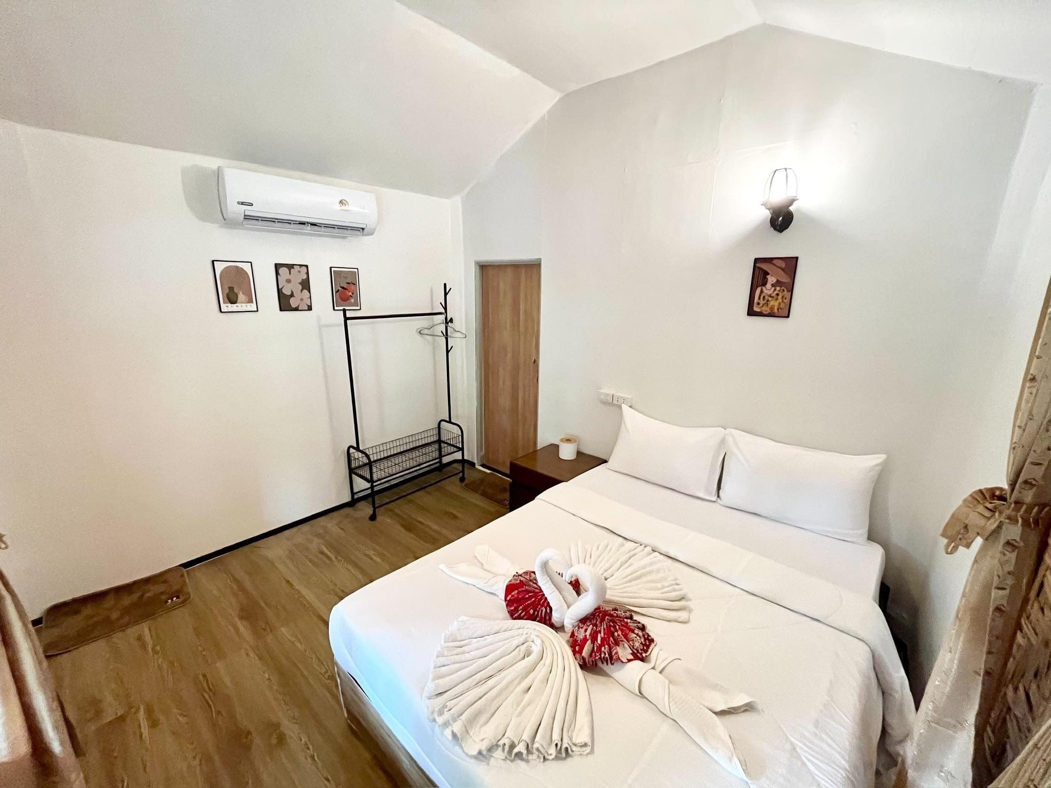 A hotel room with a bed, a coat rack, an air conditioning unit, and a wall-mounted light fixture.