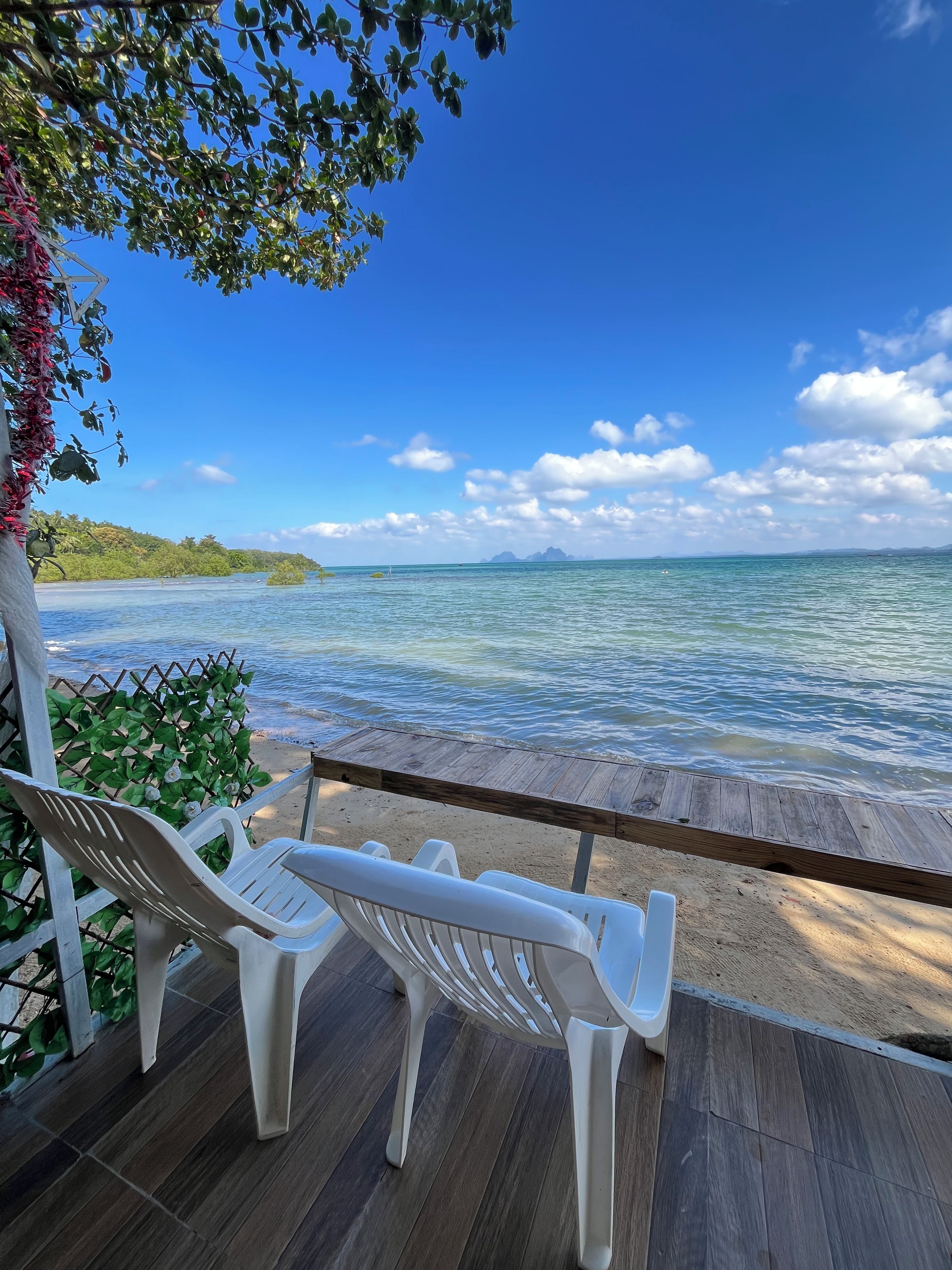 A wooden deck with two white plastic chairs facing a clear blue sea and distant land.
